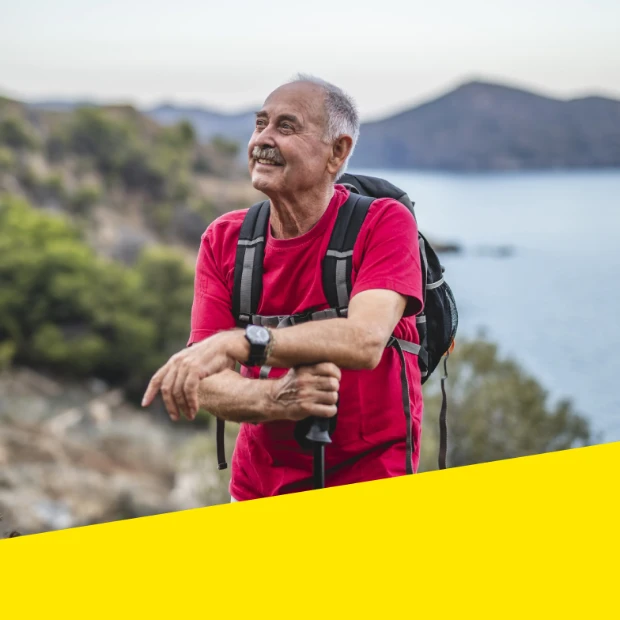 Older man rests during a hike, enjoying the mountain and lakefront scenery