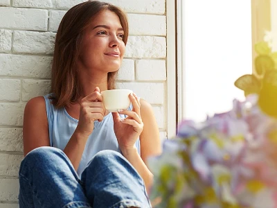 Kobieta siedzi przy oknie, pijąc ciepły napój