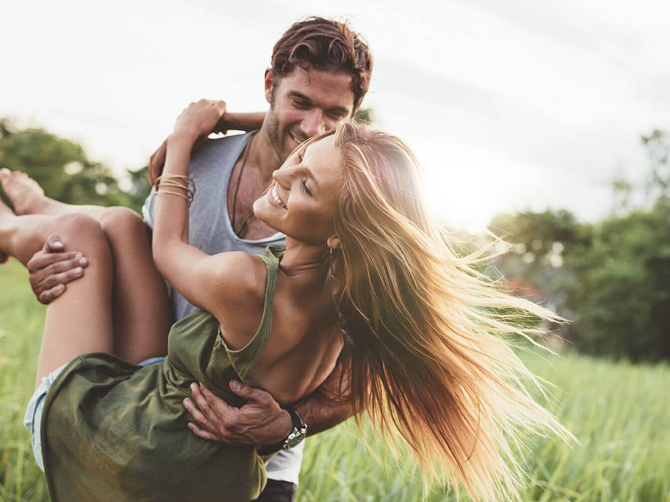 A man carrying a woman with long blonde hair through a grassy field.