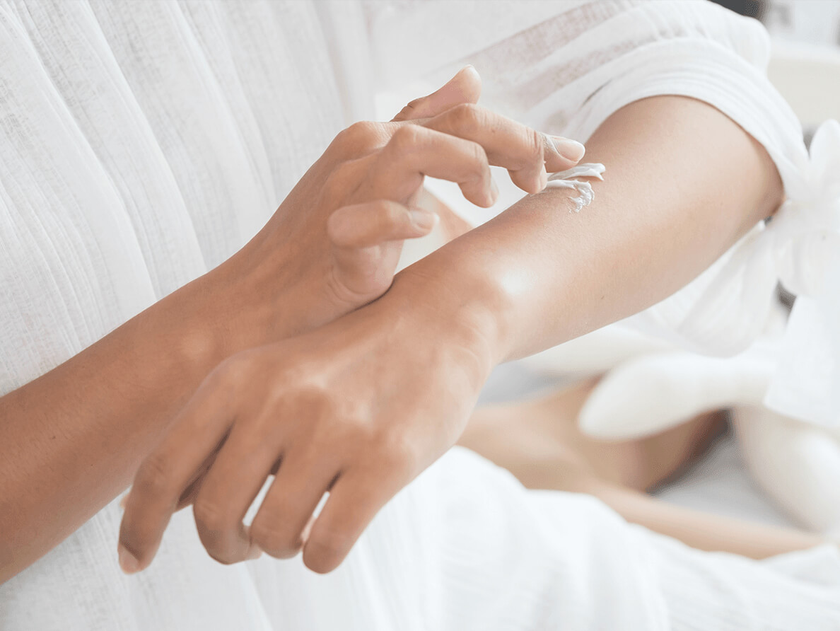 A woman rubs a white cream into her forearm.
