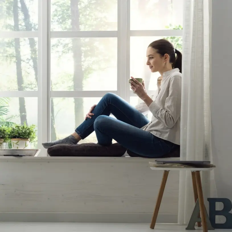 Kobieta z kubkiem herbaty siedząca na parapecie
